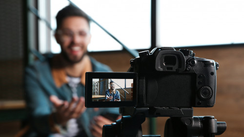 Young blogger recording video indoors, focus on camera screen