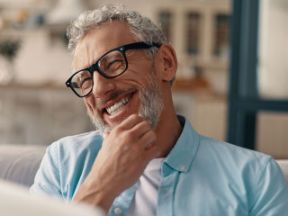 Cheerful senior man in casual clothing and eyeglasses using lapt