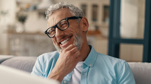 Cheerful senior man in casual clothing and eyeglasses using lapt