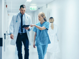 Female Surgeon and Doctor Walk Through Hospital Hallway, They Co