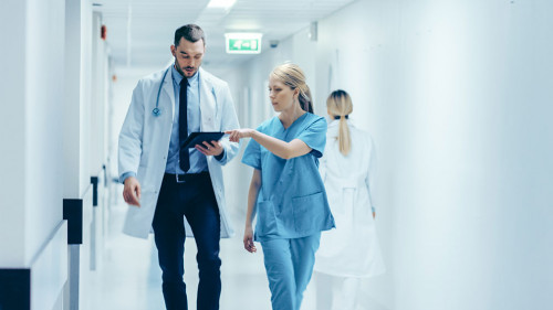 Female Surgeon and Doctor Walk Through Hospital Hallway, They Co