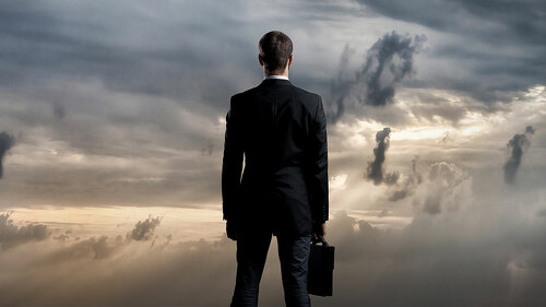 Businessman with briefcase standing over dark, dramatic ocean ba