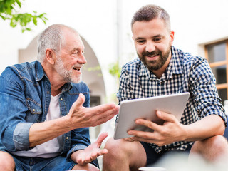 An adult hipster son with tablet and senior father in a cafe in town.