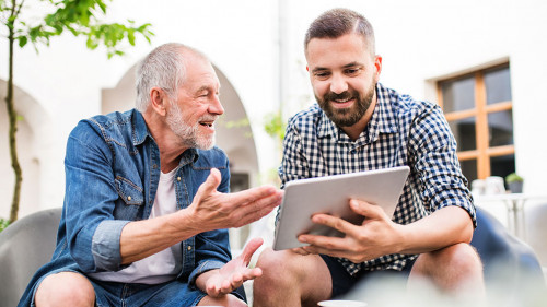 An adult hipster son with tablet and senior father in a cafe in town.