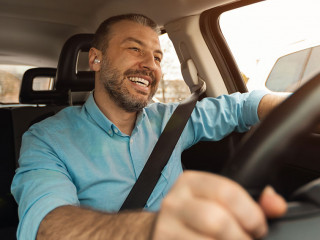 Happy man in earphones enjoying music driving luxury car