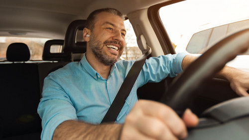 Happy man in earphones enjoying music driving luxury car