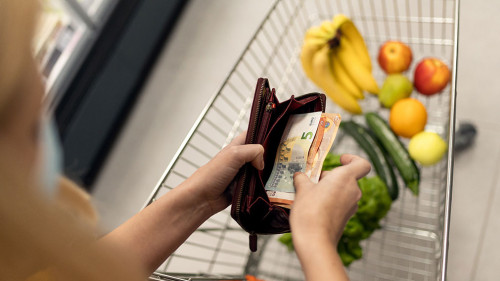 Worried woman checking her wallet when shopping in supermarket. Inflation and economic recession concept.