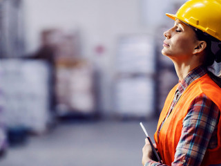 Tired female worker with tablet in hands leaning on shelf and ta