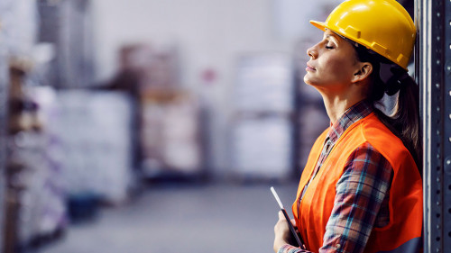 Tired female worker with tablet in hands leaning on shelf and ta