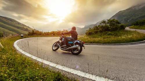 Motorcycle driver riding in Alpine landscape.