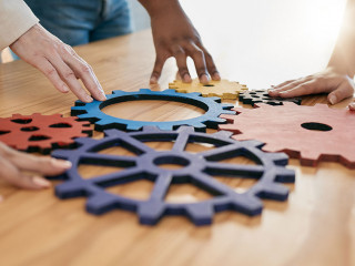 Hands, collaboration and gear with a business team working together in synergy for innovation at a workshop. Meeting, teamwork and creative with a man and woman employee group at work in the office