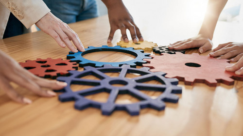 Hands, collaboration and gear with a business team working together in synergy for innovation at a workshop. Meeting, teamwork and creative with a man and woman employee group at work in the office