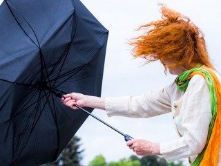 eine Frau mit roten Haaren versucht ihren Regenschirm festzuhalt