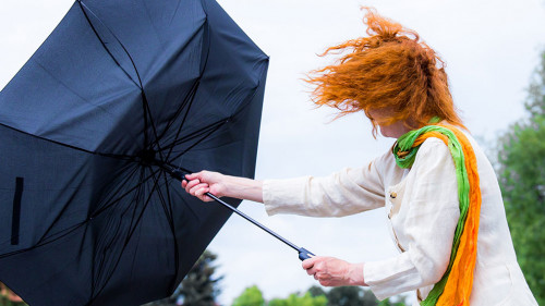 eine Frau mit roten Haaren versucht ihren Regenschirm festzuhalt