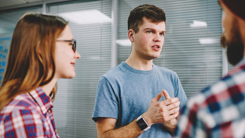 Serious hipster guy explaining study process to male and female