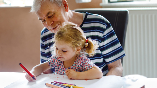 Cute little baby toddler girl and handsome senior grandfather painting with colorful pencils at home. Grandchild and man having fun together