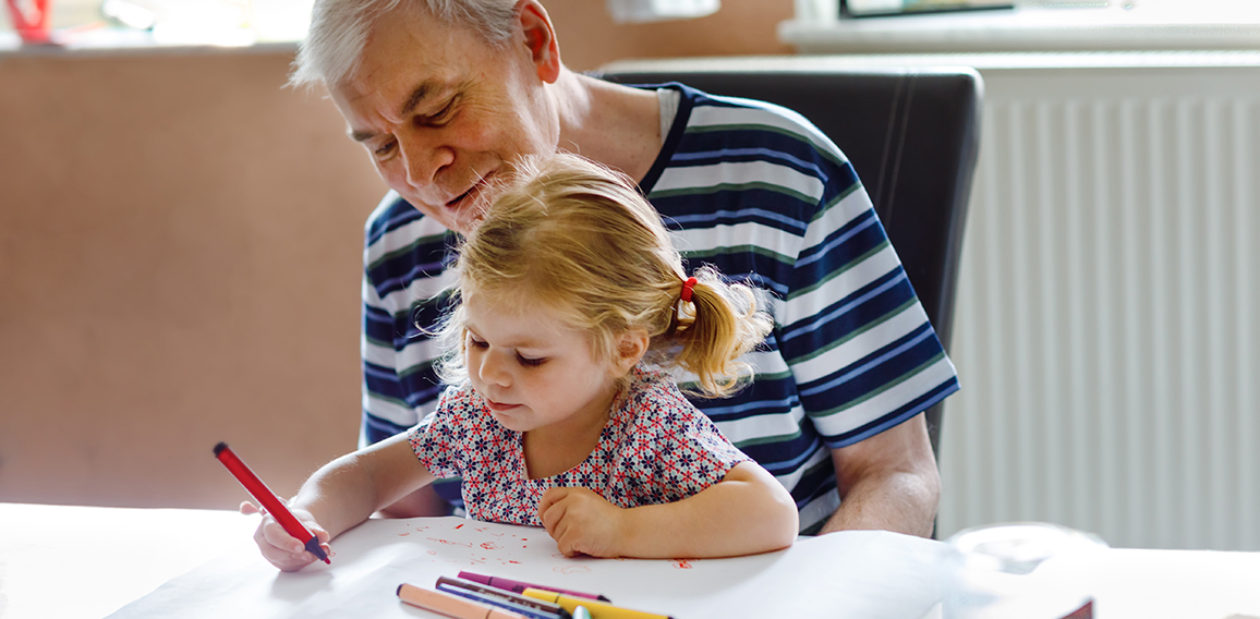Cute little baby toddler girl and handsome senior grandfather painting with colorful pencils at home. Grandchild and man having fun together
