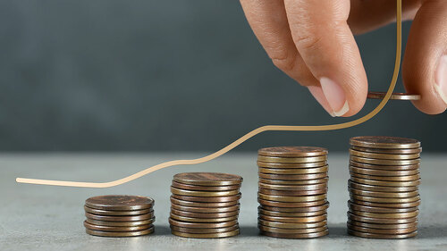 Salary increase concept. Woman stacking coins on grey table and