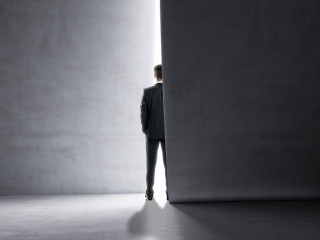Back view of man stepping into the light from behind a concrete wall. Success and future concept.