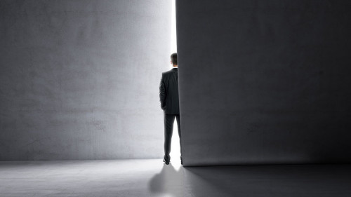 Back view of man stepping into the light from behind a concrete wall. Success and future concept.
