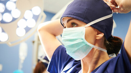 Side view of young female surgeon tying her surgical mask
