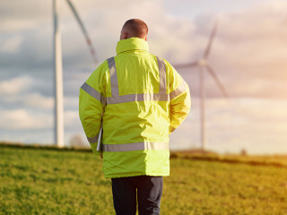 Back view of young male engineer in a wind turbine farm in the b