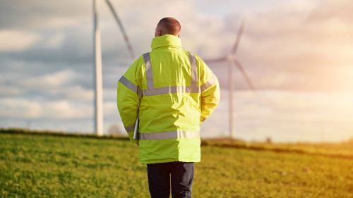 Back view of young male engineer in a wind turbine farm in the b