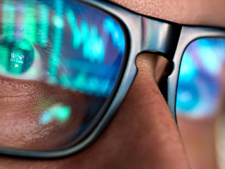 Trader looking at computer screen analyzing trading chart reflecting in glasses.