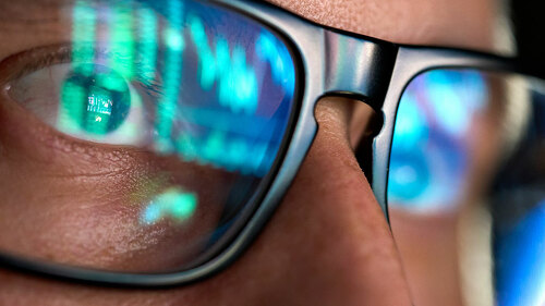 Trader looking at computer screen analyzing trading chart reflecting in glasses.