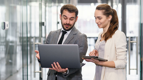 Businesswoman and businessman in laptop standing and discussing project in empty office windows with city view.