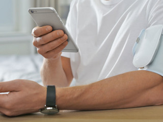 Man checking blood pressure with modern monitor and smartphone a