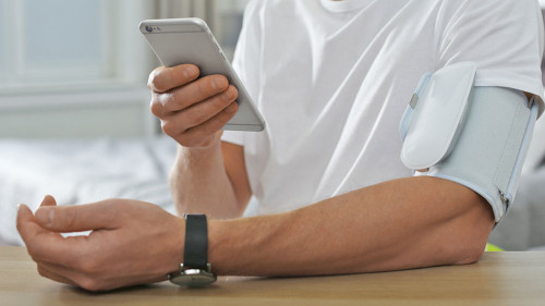 Man checking blood pressure with modern monitor and smartphone a