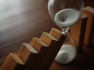 domino effect concept with wooden tiles blocked by hourglass wit