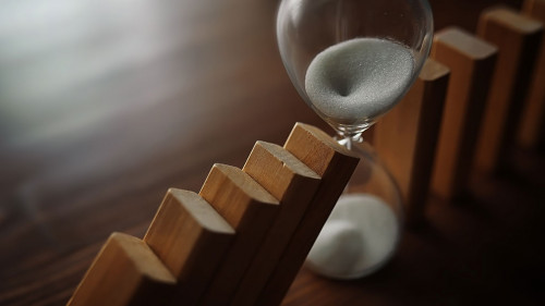 domino effect concept with wooden tiles blocked by hourglass wit