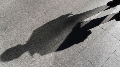 Dark shadow of a lonely person on the ground in the street. Stranger with a cigarette. Anxiety, depression, loneliness, fear concept.