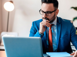 Young manager sitting at desk in bright office, working on lapto