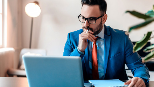 Young manager sitting at desk in bright office, working on lapto