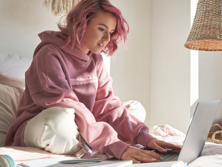 Hipster teen girl student with pink hair using laptop online learning in bed.