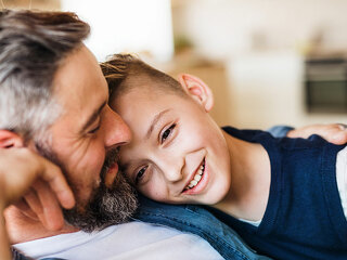 Mature father with small son sitting on sofa indoors, resting.