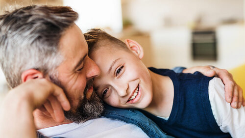 Mature father with small son sitting on sofa indoors, resting.
