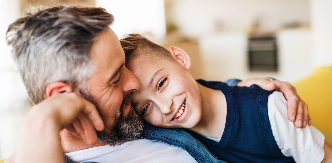 Mature father with small son sitting on sofa indoors, resting.