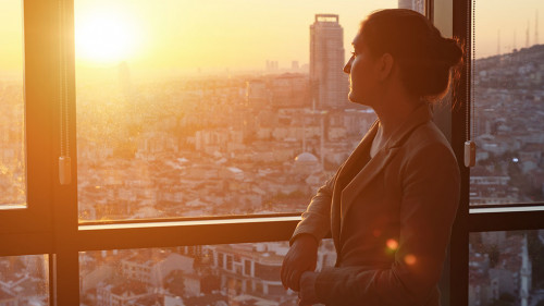 Young businesswoman in office standing near the window with panoramic city view.