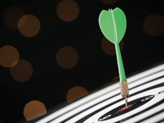 Green arrow hitting target on dart board against blurred lights.