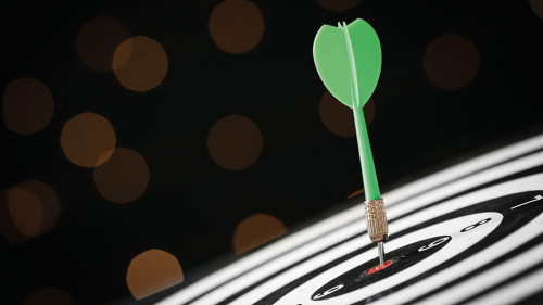 Green arrow hitting target on dart board against blurred lights.