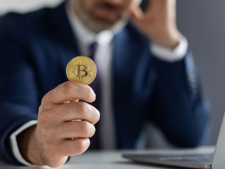 Crypto Failure. Upset Businessman Holding Bitcoin While Sitting At Desk With Laptop