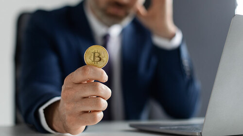 Crypto Failure. Upset Businessman Holding Bitcoin While Sitting At Desk With Laptop