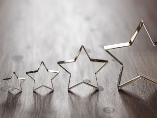 Rating - five transparent acrylic glas stars in different sizes arranged by size on a wooden table. Selective focus and copy space.