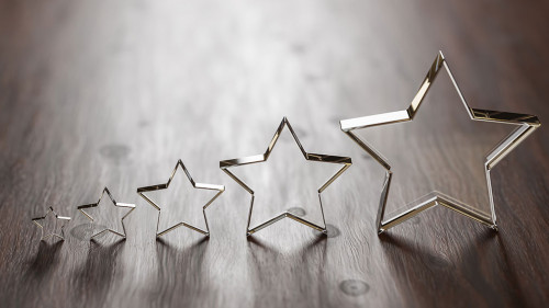 Rating - five transparent acrylic glas stars in different sizes arranged by size on a wooden table. Selective focus and copy space.