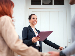 Real estate agent near door inviting young couple to enter house