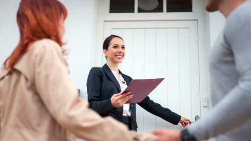 Real estate agent near door inviting young couple to enter house